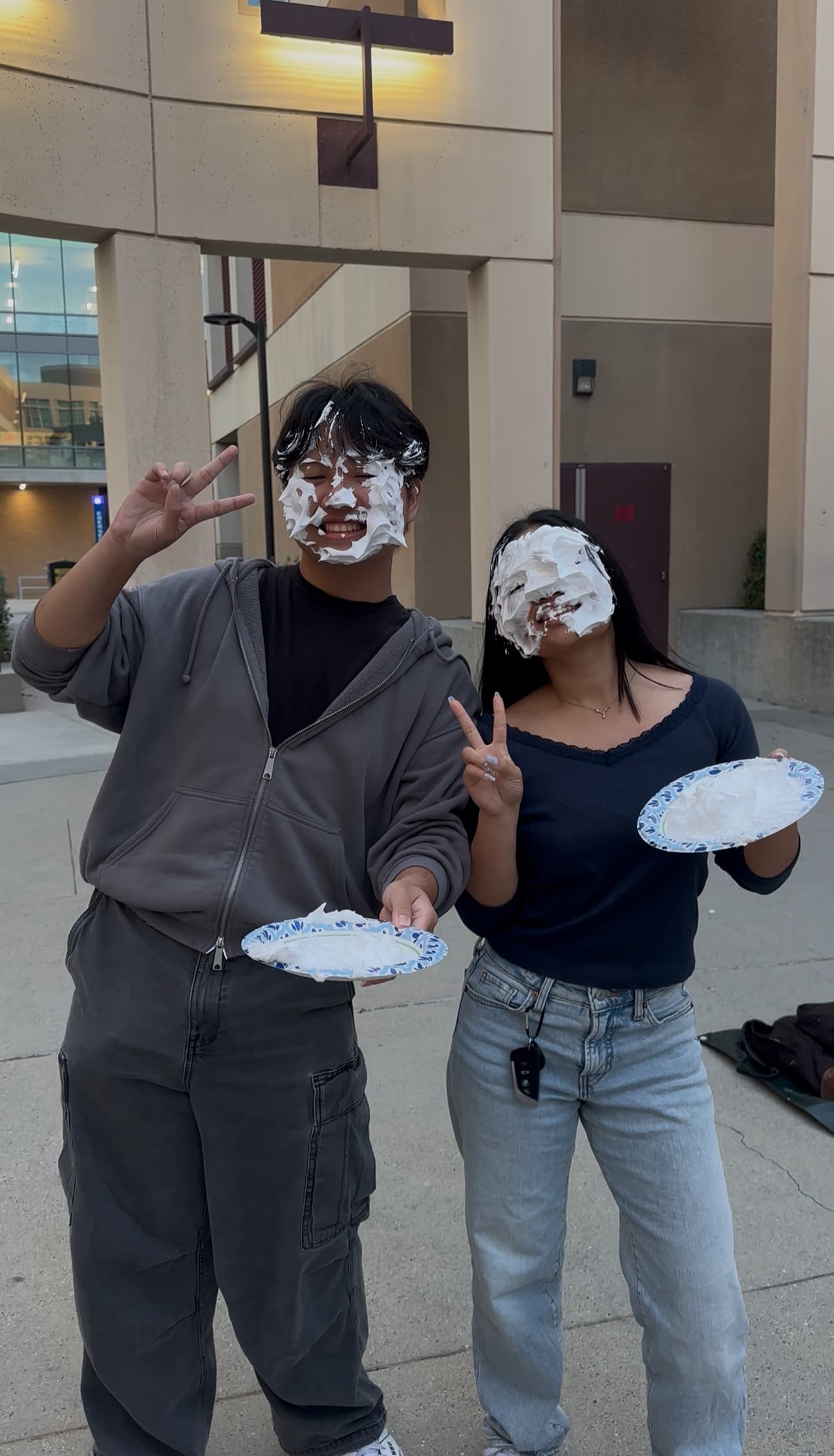 Two PACT members with whipped cream on their faces holding pie plates at Pie-a-PACTer