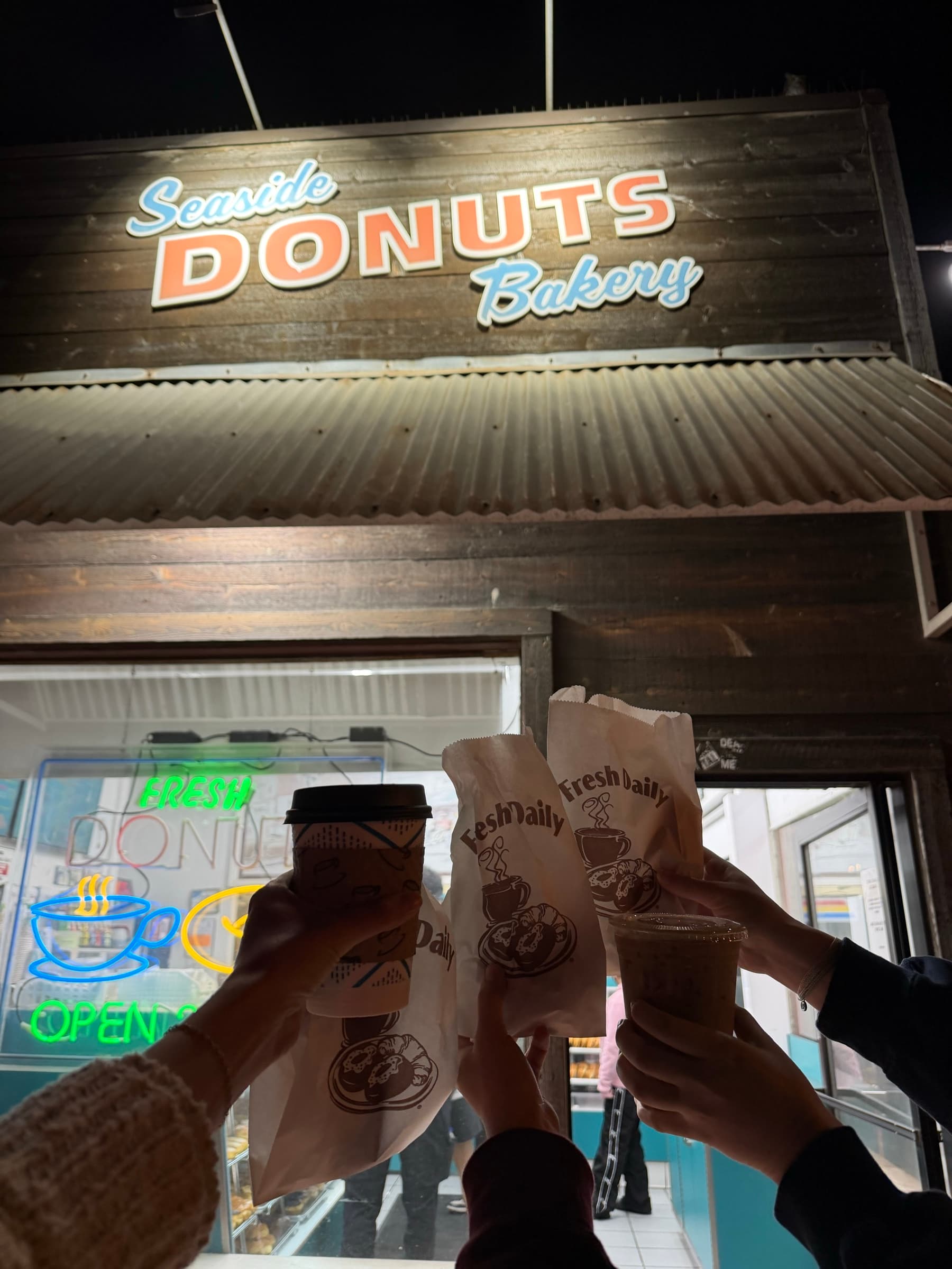 PACT members toasting coffee and pastry bags outside Seaside Donuts at night
